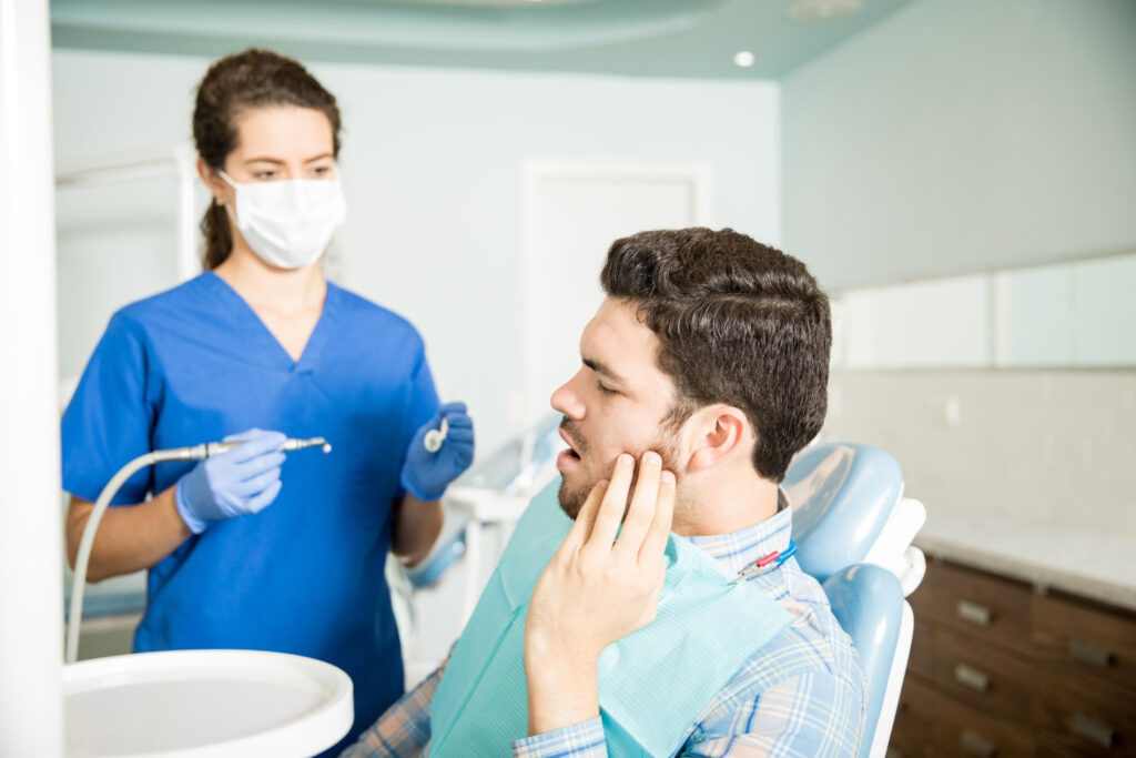 mid-adult man suffering from wisdom teeth pain while looking at a dentist
